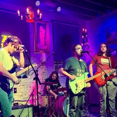 A band playing under purple and blue light, candles glowing on a chandelier above them.