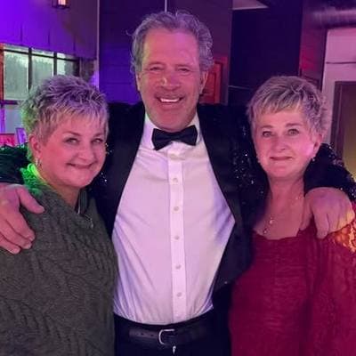Three guests dressed up for the night: a man in a tuxedo between two smiling women.