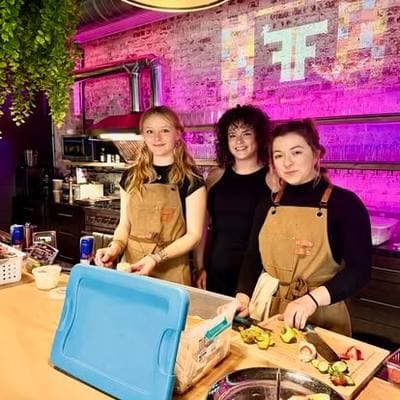 Three caterers smiling behind the counter as they prepare food.