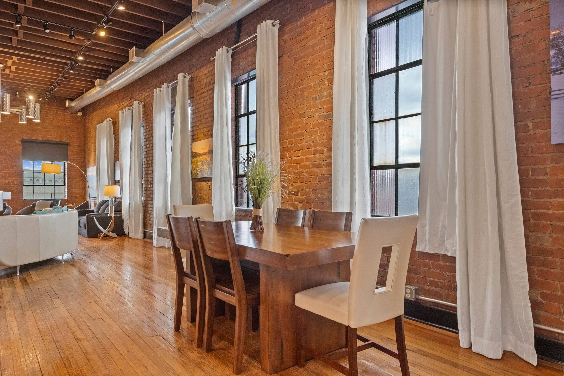 The dining table beside tall windows and exposed brick.