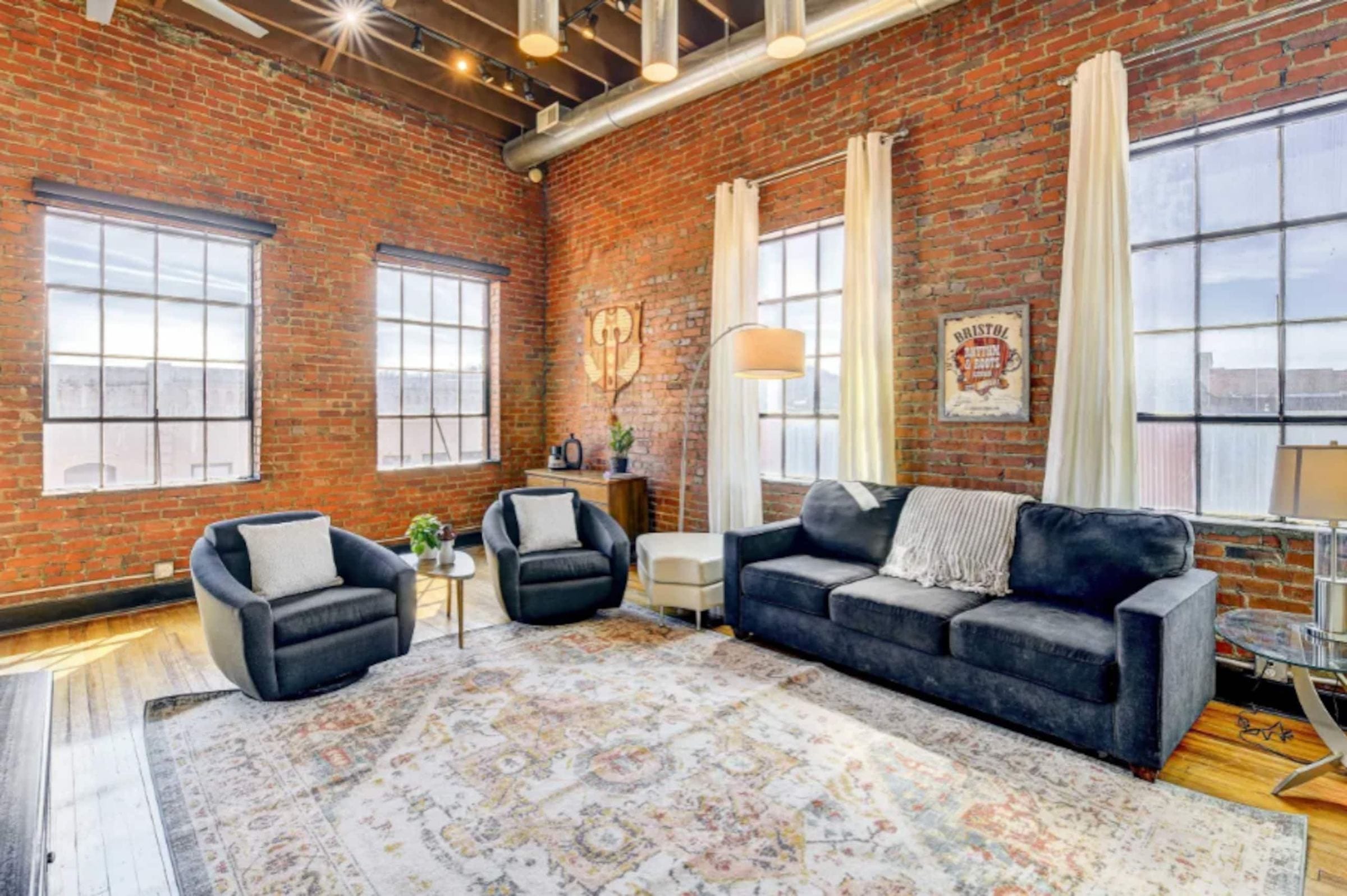 Swivel chairs and a dark sofa on a patterned rug beneath the windows.