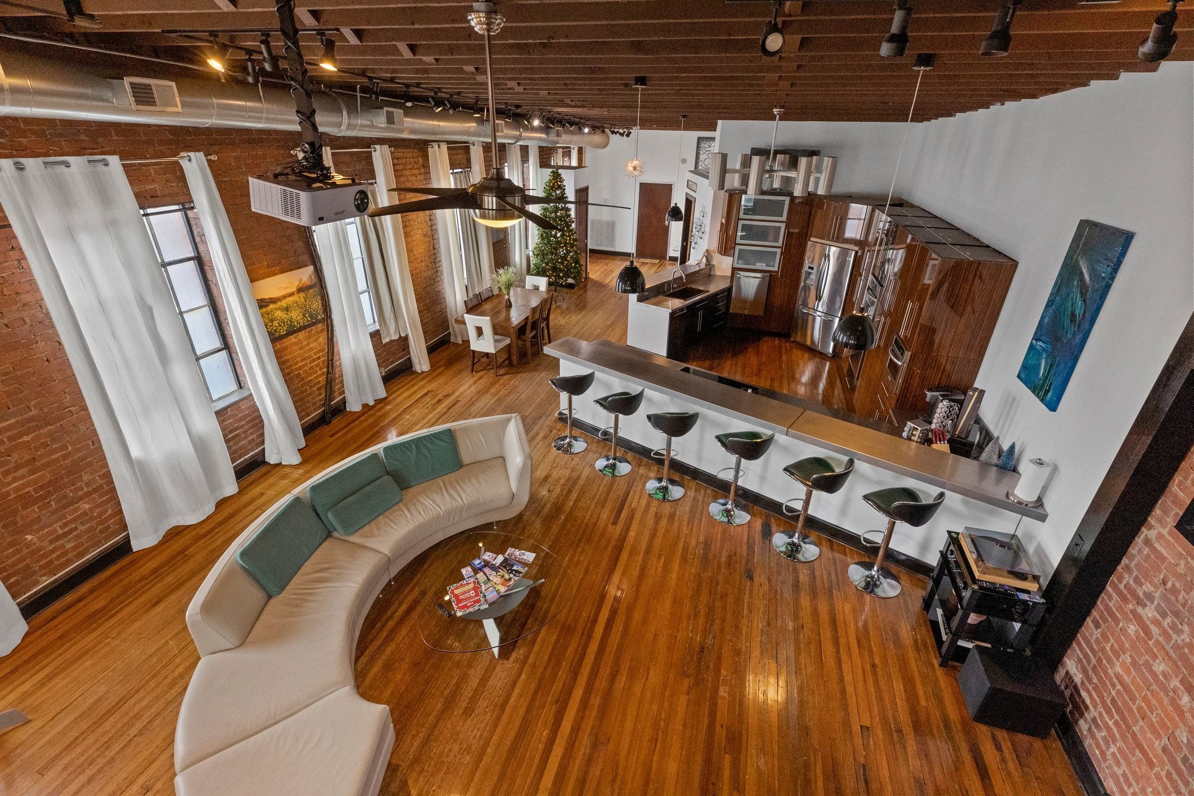 The main floor from above: the curved sofa, the bar and its stools, the dining table and the kitchen beyond.