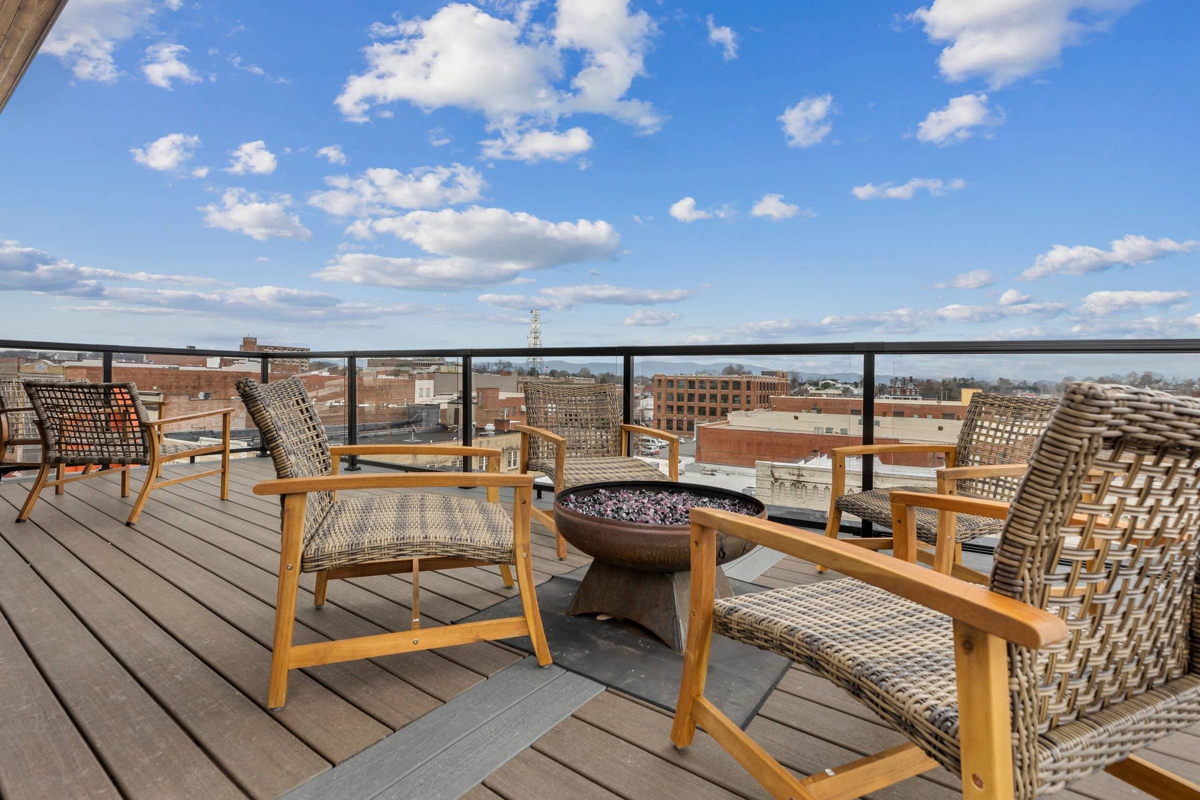 The private rooftop deck on a clear day: woven lounge chairs around a fire pit, with the rooftops and hills of downtown Bristol behind.