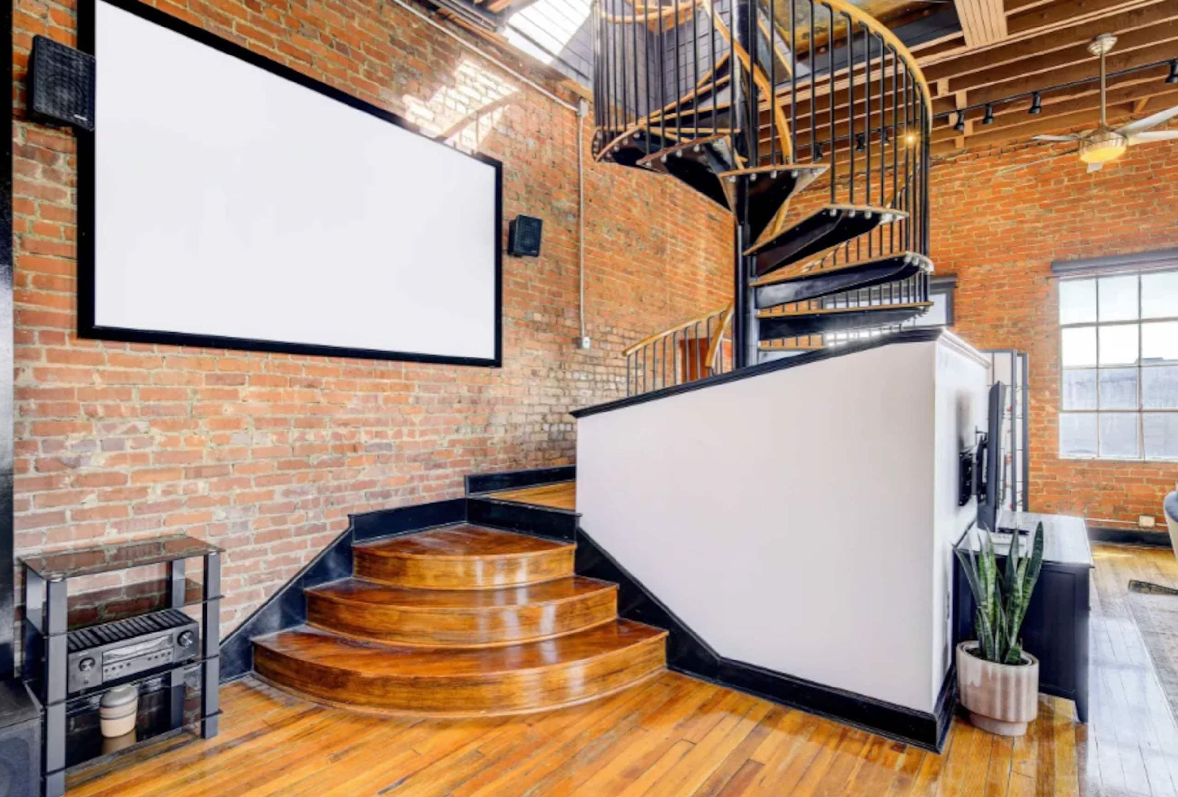 Curved wooden steps up to the spiral stair's platform, beside a projector screen.