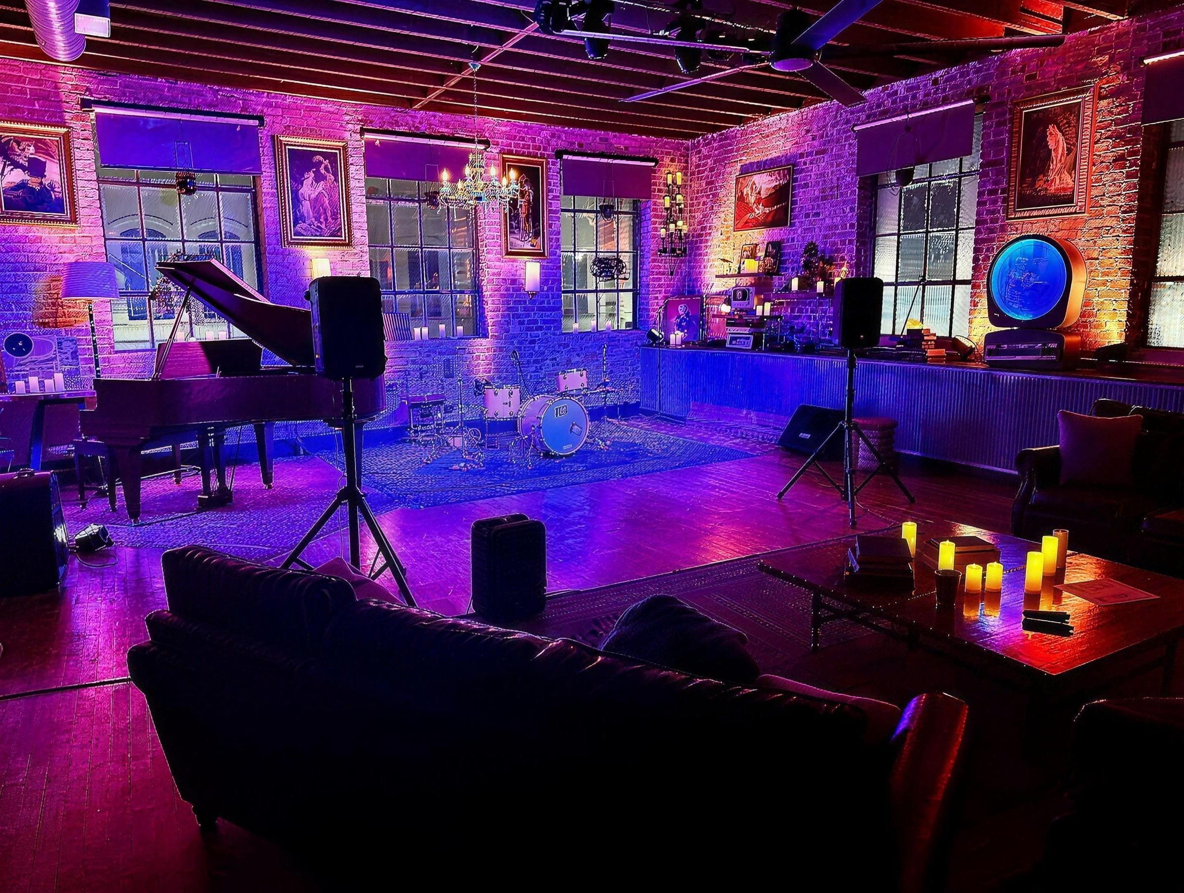 705 State set up for a show: purple and pink light on brick walls, a piano, a drum kit, speakers, and candles on the tables.