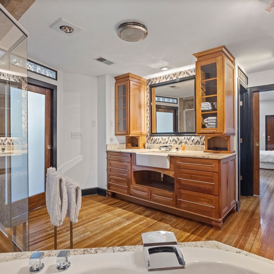 The bathroom, seen from the jacuzzi tub: a double vanity with a farmhouse sink, the glass shower at left, and the bedroom through the doorway.