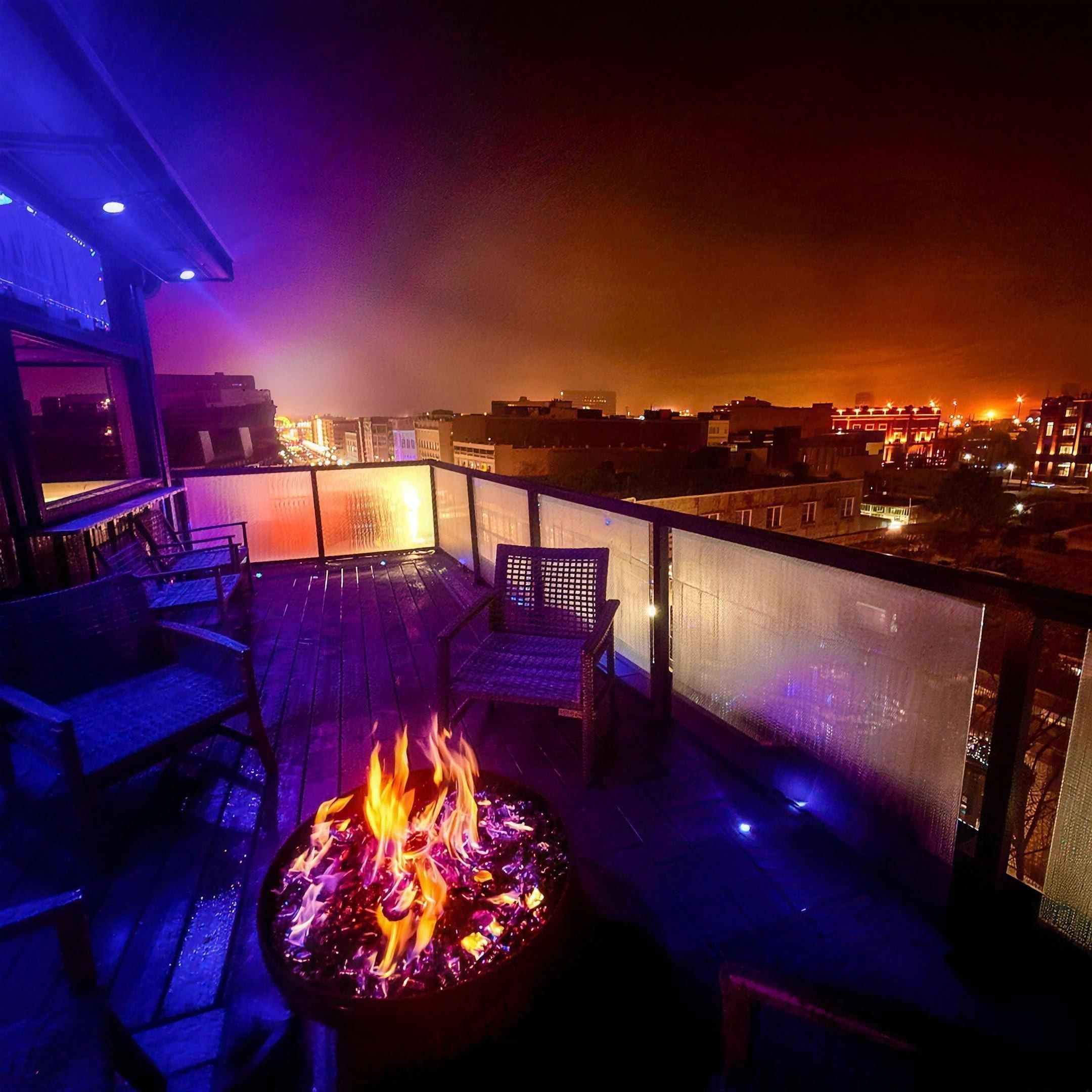 The rooftop deck at night: the fire pit lit, blue accent lights along the railing, and downtown Bristol glowing beyond it.