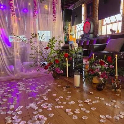 A ceremony set up inside 705 State: rose petals on a wood floor, white drapes, candles and floral arrangements against exposed brick.