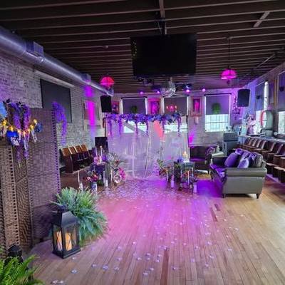 The long room dressed for an event: petals down the floor, drapes, lounge seating along the brick wall.