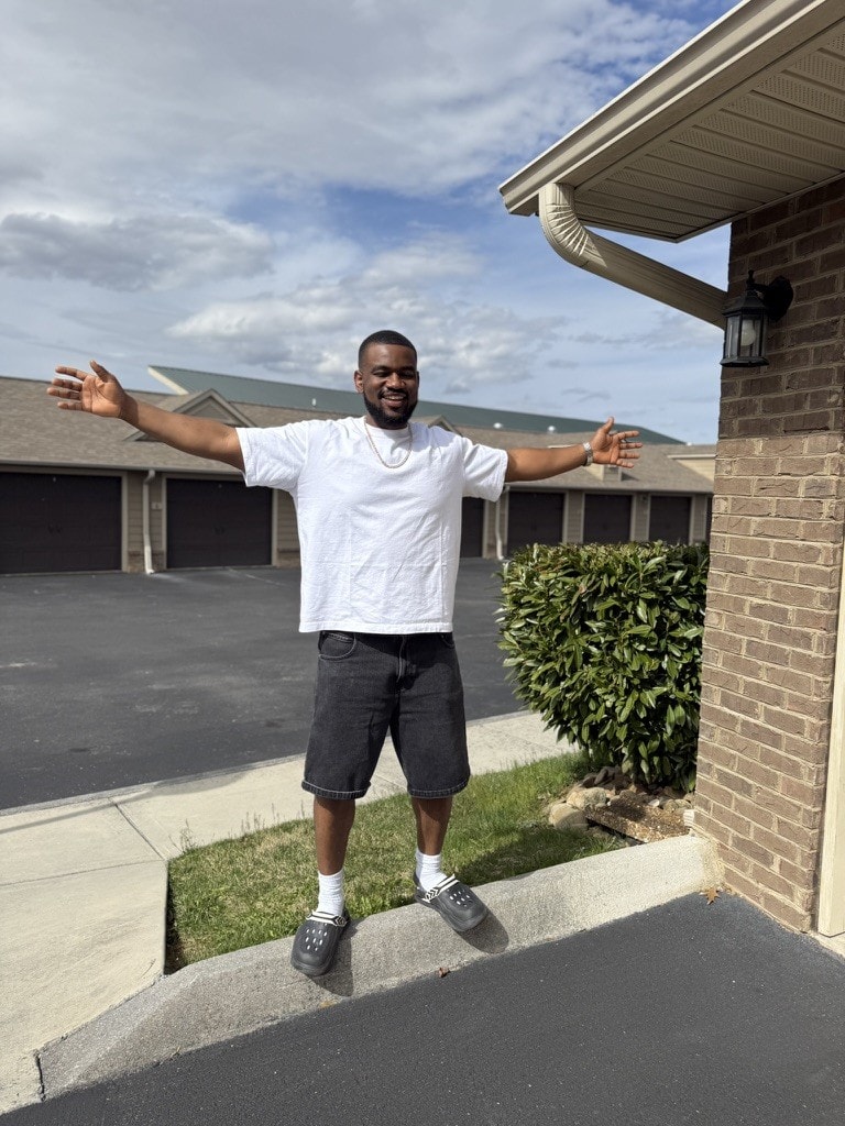 DJ Pharoh outside on a bright day, arms spread wide and smiling.